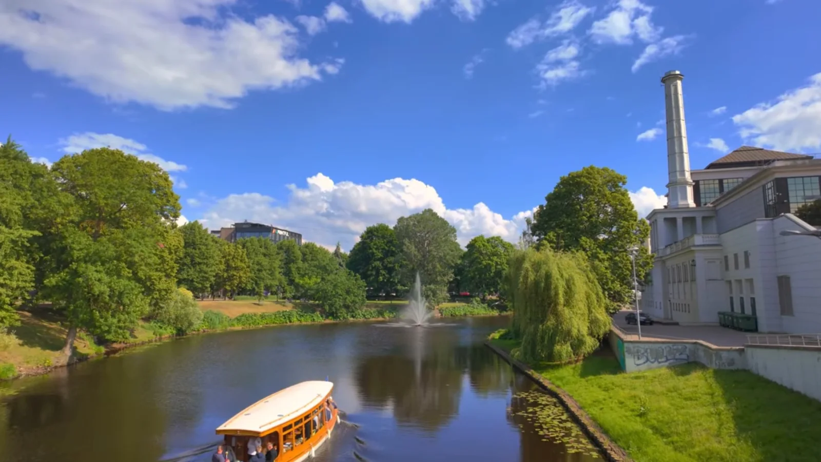 Canal boat on Riga City Canal beside green parkland under a blue sky